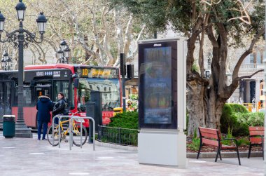Valencia, İspanya 'da modern bir şehir caddesinde halka açık bir otobüs durağı, dijital reklam panosu ve canlı bir şehir ortamında yerel halk yer alıyor. Avrupa 'da şehir taşımacılığı ve günlük yaşam.