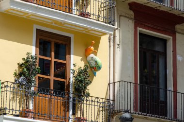 Bereketli yeşil bitkilerle dolu renkli bir balkon manzarası ve güneşli bir Avrupa şehrinde neşeli bir salyangoz heykeli mimari cazibe ve kentsel yaşam tarzını yakalıyor..