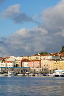 Yat limanına demirli canlı deniz manzarası, çok renkli konut binaları ve dramatik sabah bulutları. Seyahat ve mimari temalar için mükemmel.