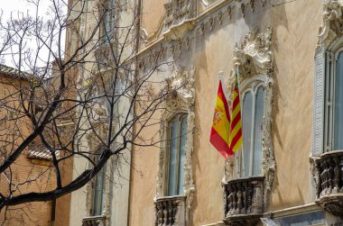 İspanya 'nın Valencia kentindeki bir barok binanın tarihi mimarisi. İlkbahar güneşinde zarif pencerelerin önünde ulusal ve bölgesel bayraklar sallanıyor..