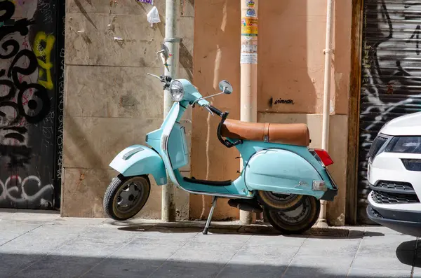Deri koltuklu klasik retro scooter, parlak güneş ışığında bir şehir caddesinde duruyor. Akdeniz atmosferini ve şehir ulaşımını çağrıştırıyor..