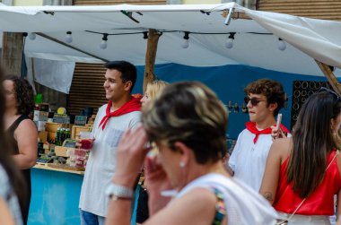 Bir grup genç yetişkin, canlı bir açık hava pazarında içki içip sosyalleşiyorlar. Esnaf tezgahları ve yaz festivali atmosferi, yaşam tarzı ve turizm konuları için mükemmel..