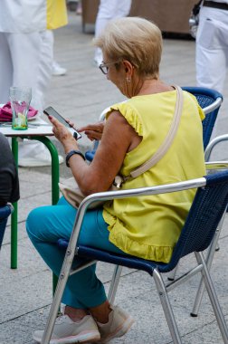 Aktif yaşlı kadın bir sokak kafesinde oturuyor, akıllı telefonuyla mesaj yazıyor ve modern şehir atmosferinin tadını çıkarıyor. Şehir hayatı, iletişim, yaşam tarzı konsepti.