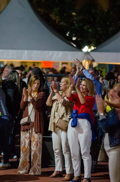 Bir grup neşeli kadın, canlı bir açık hava festivali sırasında alkış tutuyor, etkinlik çadırlarının ışıkları altında olumlu duygular ve sosyal etkileşimler sergiliyorlar..