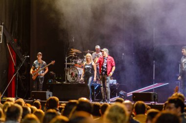 Dinamik rock grubu müzik konserinde heyecanlı seyircileri eğlendiriyor, canlı ışıklar ve dumanlı atmosfer enerjik bir canlı sahne yaratıyor.