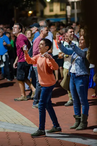 Heyecanlı kalabalık gece açık hava festivaline katılıyor, akıllı telefonlarda anları yakalıyor, neşeli atmosfer ve topluluk ruhuyla çevrili..