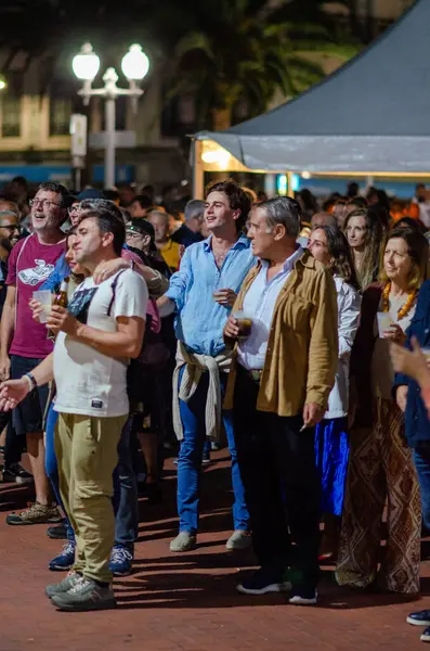 Bir gece açık hava etkinliğine katılan, şehir ışıkları altında canlı müzik dinleyen, sosyalleşen, neşeli atmosfer ve pozitif duygular yaşayan bir grup insan..