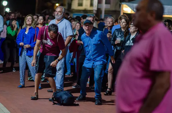 Bir akşam sokak festivalinde müzik, dans ve canlı şehir gece hayatı atmosferiyle kutlama yapan geniş bir grup insan..