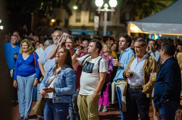 Canlı bir grup insan, şehir ışıkları altında sosyalleşmek ve içkilerin tadını çıkarmak için bir açık hava festivalinde toplandı. Şehir gece hayatı, grup etkinlik ortamı.