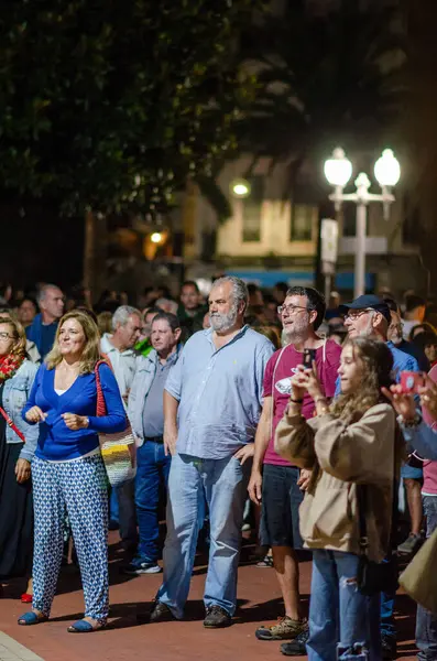 Bir grup yetişkin, gece şehir parkında sokak lambalarıyla aydınlatılmış bir açık hava etkinliğinin tadını çıkarıyorlar. Şehir halkı, gece toplantısı..