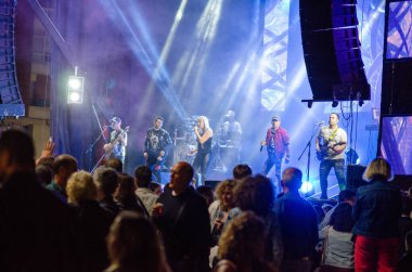 Açık hava müzik festivalinde parlak bir sahnede dinamik canlı grup performansı. Kalabalıktaki insanlar enerjik atmosferin ve aydınlatılmış gece etkinliğinin tadını çıkarıyorlar..