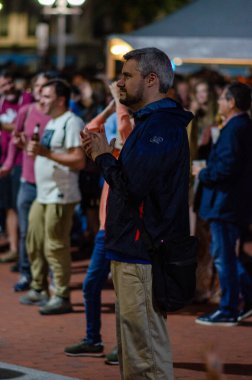 Canlı bir sokak etkinliğinde ayakta duran ve alkışlayan bir adamın samimi çekimleri, gece neşeli bir kalabalık tarafından çevrelenmiş, kentsel bir ortamda. Kutlama ve gece hayatı kavramları için mükemmel..
