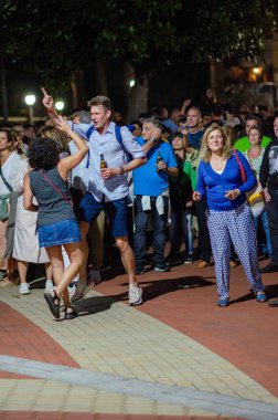 Neşeli kalabalık dans ve müzikle açık hava festivalinin keyfini çıkarıyor, sosyal toplantıların ve yerel etkinliklerin heyecanını yakalıyor..