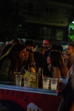 İnsanlar bir gece festivali sırasında canlı bir açık hava barında sosyalleşir ve birlikte içmekten zevk alırlar. Şenlikli atmosfer, şehir gece hayatı, hafta sonu eğlencesi.