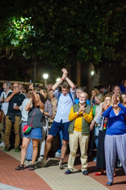 Çeşitli yetişkinlerden oluşan canlı bir grup, heyecan ve coşku göstererek bir gece açık hava konserinde toplandı. Alkışlayın, şarkı söyleyin ve festival atmosferinin tadını çıkarın..