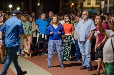 Farklı yaşlardaki insanlar, gece bir şehir parkında açık hava etkinliğinin keyfini çıkararak, canlı eğlence ve topluluk atmosferini deneyimlerler..