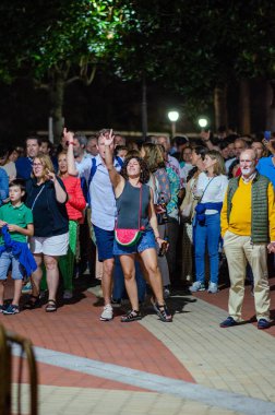 Bir açık hava festivalinde sosyalleşen ve kutlama yapan heyecanlı kalabalık, neşeli ifadeler, yaz modası ve canlı şehir enerjisiyle.