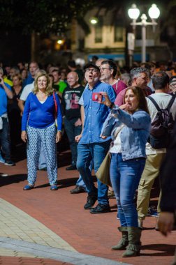Bir şehir parkında, açık havada eğlenen yetişkinlerden oluşan çeşitli bir kalabalık şehir ışıkları altında samimi duygular ve sosyal etkileşimler yakalıyor..