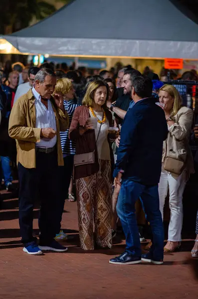 Yetişkinlerden oluşan büyük bir grup gece dışarıda toplanıyor, canlı bir festivalde ya da şehir etkinliğinde sosyalleşiyorlar ve içkilerinin tadını çıkarıyorlar. Şehir kutlama atmosferi, samimi insanlar, gece hayatı.