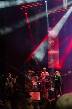 Sahnede karizmatik bir kadın vokalist, canlı kırmızı spot ışıkları ve müzik konserinde enerjik bir kalabalık atmosferi olan bir rock grubunun dinamik canlı performansı..