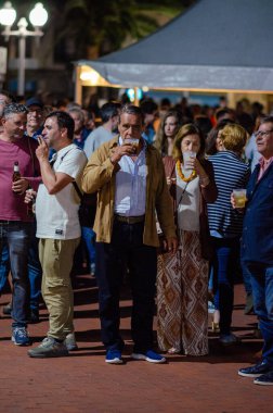 İnsanlar canlı bir gece sokak festivalinde, açık havada içki içip sohbet ediyorlar. Şehir gece hayatı ve kutlama havası.