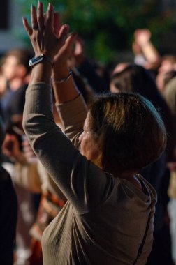 Bir açık hava festivali sırasında coşkulu bir kalabalığın içinde ellerini kaldırmış enerjik bir kadın, coşkulu bir halk toplantısında neşe ve kutlama yapıyor..