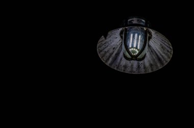 Yıpranmış metal bir gölgesi olan, kumlu bir endüstriyel LED lambaya yakın çekim, karanlıkta aydınlatma, kentsel veya grunge arka plan ve dramatik ışıklandırma kavramları için mükemmel..