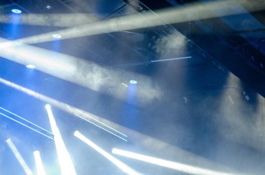 Sahnede parlak spot ışıkları ve atmosferik dumanla dinamik bir sahne, çağdaş bir mekanda konserler, partiler veya etkinlikler için enerjik bir ortam yaratıyor..