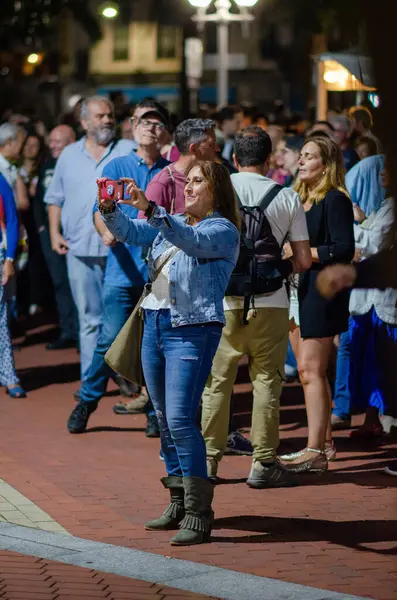 Gülümseyen bir kadın, canlı bir açık hava festivali sırasında, çeşitli kalabalık ve şehrin ışıkları altında enerjik bir şehir atmosferi yaratan bir selfie çekiyor..