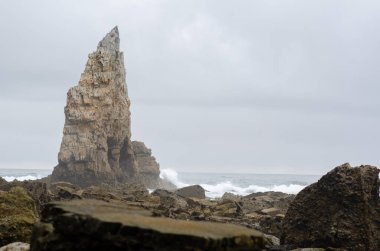 Kasvetli ve bulutlu bir günde kayalık sahilden yükselen dalgalar kayalıklara çarpıyor. Doğa, macera ve seyahat kavramları için mükemmel..