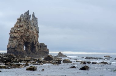 Bulutlu bir gökyüzünün altında kayalık kıyılarla çevrili muhteşem bir deniz yığını yükseliyor. Sakin deniz manzarası, doğal dönüm noktası, dramatik kıyı şeridi..