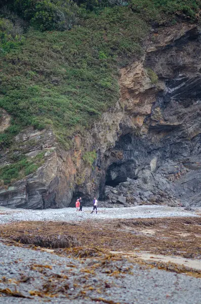 Üç kişi, vahşi yeşillik ve doğal kaya oluşumlarıyla çevrili dramatik uçurumların dibinde manzaralı bir çakıl taşı plajını keşfediyor. Doğa ve macera temaları için mükemmel..