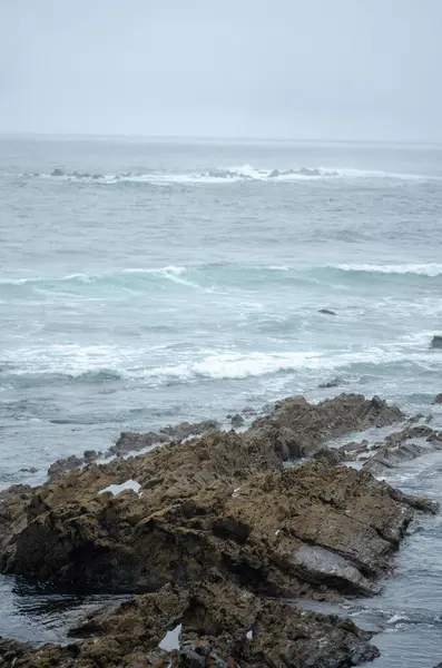 Bulutlu bir gökyüzü altında çarpışan dalgalarla vahşi kayalıklar sakin ve dramatik okyanus manzarasını yakalar. Seyahat ve doğa kavramları için idealdir..