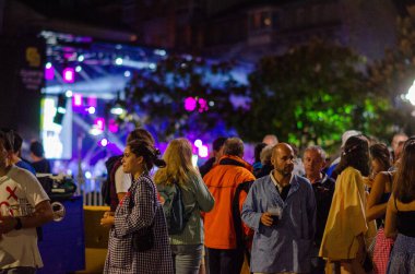 Açık hava müzik festivalinde renkli ışıklar altında sosyalleşen geniş bir grup, canlı bir şehir etkinliğinin enerjisini, kültürünü ve heyecanını yakalıyor..