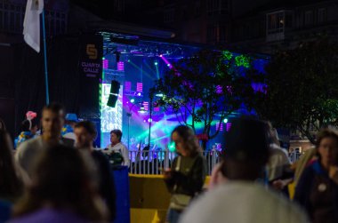 Canlı bir şehir ortamında renkli sahne ışıkları altında insanların konser verdiği açık hava müzik festivalinde canlı bir gece sahnesi..