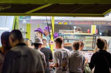 Yoğun bir yemek kamyonu, gece açık hava festivalinde çeşitli gençlere hizmet veriyor. Lezzetli sokak yemekleri seçenekleri ile canlı ve sosyal bir atmosfer yaratıyor..