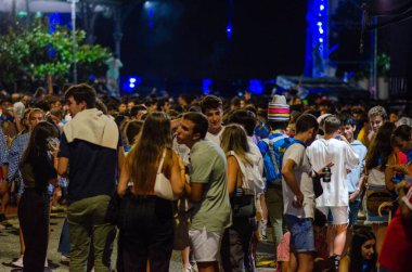 Genç yetişkinlerden oluşan canlı bir kalabalık, bir sokak festivalinde kutlama yapmak ve sosyalleşmek için gece dışarıda toplanıyor. Parlak ışıklar ve enerjik ruh hali şenlikli bir şehir manzarası yaratır..