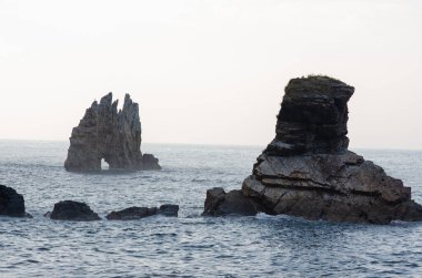 Sakin okyanus sularından dramatik deniz kayaları oluşumları yükselir, sakin ve manzaralı bir kıyı manzarası yaratarak seyahat ve doğa arka planları için idealdir..