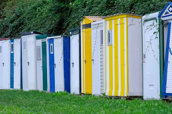 Parlak boyanmış plaj kulübeleri yeşil bir çitin önünde dizilmiş, canlı bir yaz atmosferi yaratıyor ve rahatlama ve tatil havası yaratıyor..