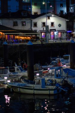 Samimi bir limanda gece hayatı. Parlayan bir sahil restoranının önüne yanaşmış küçük botlar ve canlı, atmosferik bir manzara yaratan klasik binalar..