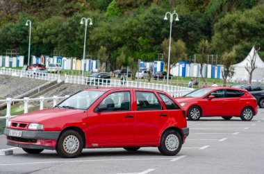 Ön planda kırmızı bir araba ve arka planda yeşil ve şehir altyapısı, ulaşım ve seyahat kavramı ile çevrili başka bir araba olan şehir otoparkı..