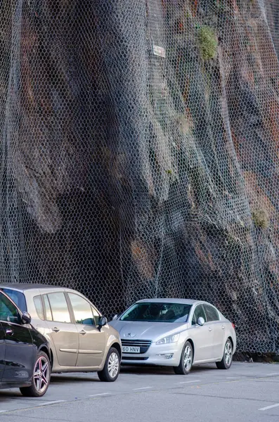 Dik bir uçurumun kenarına park edilmiş birkaç araba kaya düşüşü koruması için tel örgüyle korunuyor. Kentsel güvenlik altyapısı ve risk önleme kavramı.