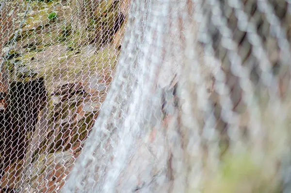 Kayalık bir yamaçta heyelan koruması için kurulmuş metal ağ çitleri üzerine seçici bir odak noktası. Görüntü, güvenlik ve çevre bakımını iletir.