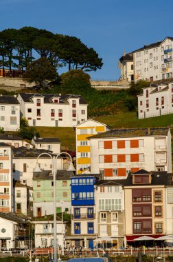 Yeşil bir yamaçta, sıcak güneş ışığıyla yıkanmış canlı evlerin olduğu büyüleyici sahil manzarası. Seyahat, mimari ve yaz yaşam tarzı temaları için ideal.