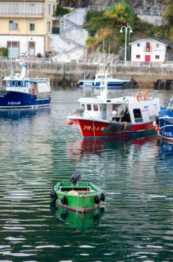 Renkli balıkçı teknelerinin kıyıya yanaştığı huzurlu bir liman sahnesi, geleneksel bir Avrupa kıyı köyünün atmosferini yansıtıyor..