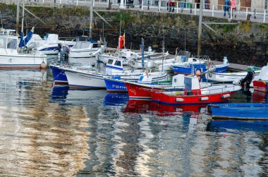 Huzurlu bir limanda yüzen demirli balıkçı tekneleri taş rıhtımının yakınındaki sakin sulara yansıyor. Seyahat, turizm ve deniz teması için ideal.