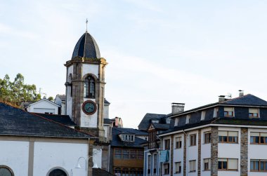 Günbatımında huzurlu bir Avrupa köyünde, çatıların üzerinde yükselen büyüleyici eski saat kulesi klasik mimari ve sakin şehir manzarasını yakalıyor..