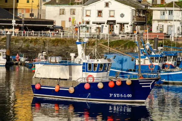 Canlı, mavi bir balıkçı teknesi, küçük bir İspanyol sahil kasabasının otantik atmosferini yansıtan, güzel bir limana demirlemiş..
