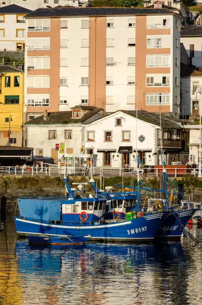 Yat limanına yanaşan geleneksel mavi balıkçı tekneleri, deniz kültürü ve canlı liman mimarisini ön plana çıkaran pitoresk bir sahil kasabasındaki yerel yaşamı yansıtıyor..