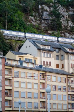 Şehir manzarası, şehir dairelerinin üstündeki viyadük bir trenle seyahat eden, yemyeşil ve kayalık yamaçlarla çevrili, dinamik şehir yaşamını yakalayan,.